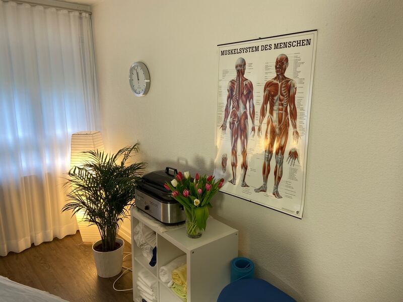 Behandlungsraum mit Pflanzen und einem Plakat des menschlichen Muskelsystems.